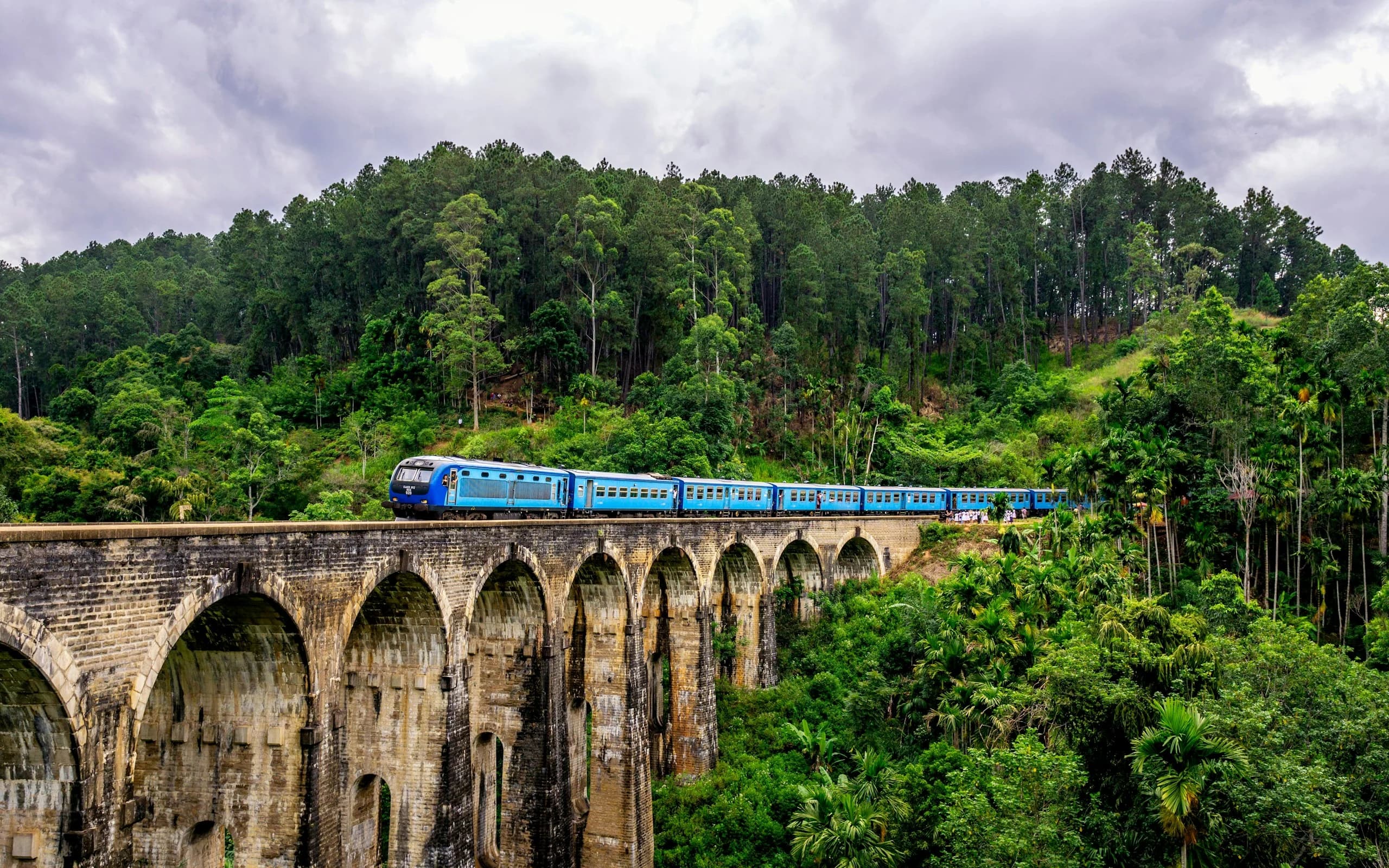 A blue train winding across the Nine Arch Bridge in Ella, Sri Lanka